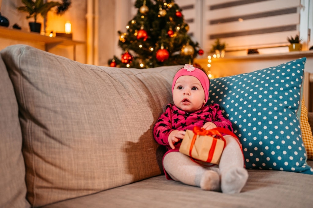Cute little baby girl on the couch playing with Christmas present. 50 IDEAS DE REGALOS DE NAVIDAD PARA TU BEBE5